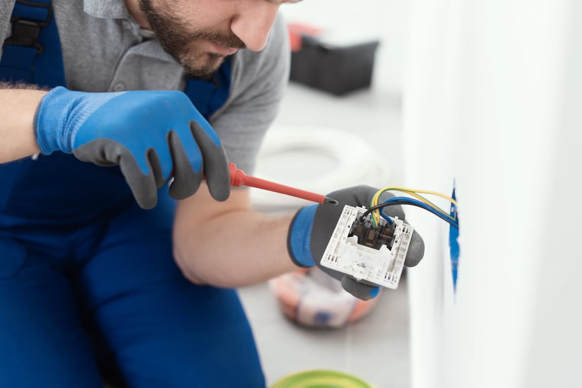 Un electricien remplace une prise de courant. Il a son habilitation électrique