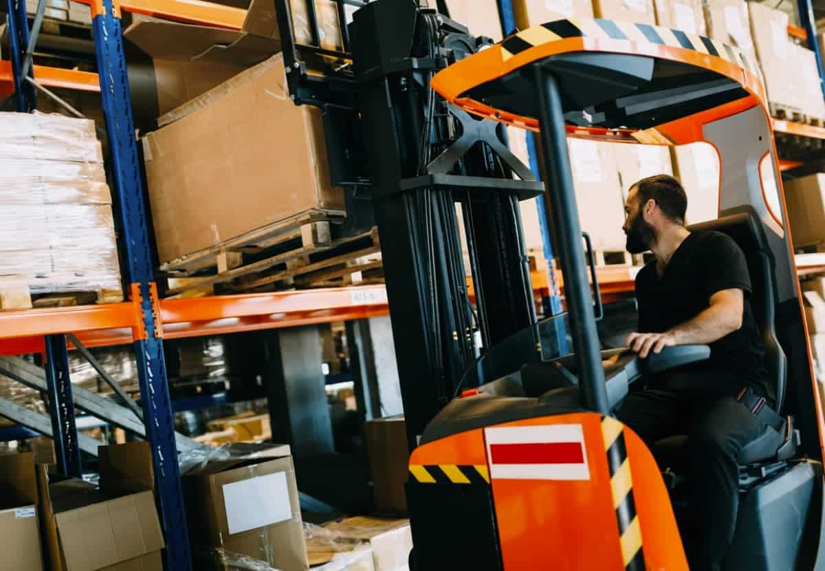 Un cariste dépose une palette dans un rack avec son chariot à mât rétractable de catégorie 5 de la R.489 CACES