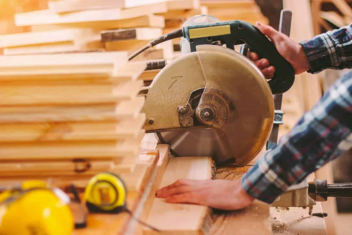 Un menuisier découpe des planches avec une scie circulaire radiale avec sa protection pour limiter les risques d'accident
