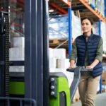Une femme conduisant un gerbeur à conducteur accompagnant pour gerber des palettes a suivi une formation sécurité pour limiter les risques