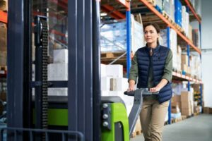 Une femme conduisant un gerbeur à conducteur accompagnant pour gerber des palettes a suivi une formation sécurité pour limiter les risques